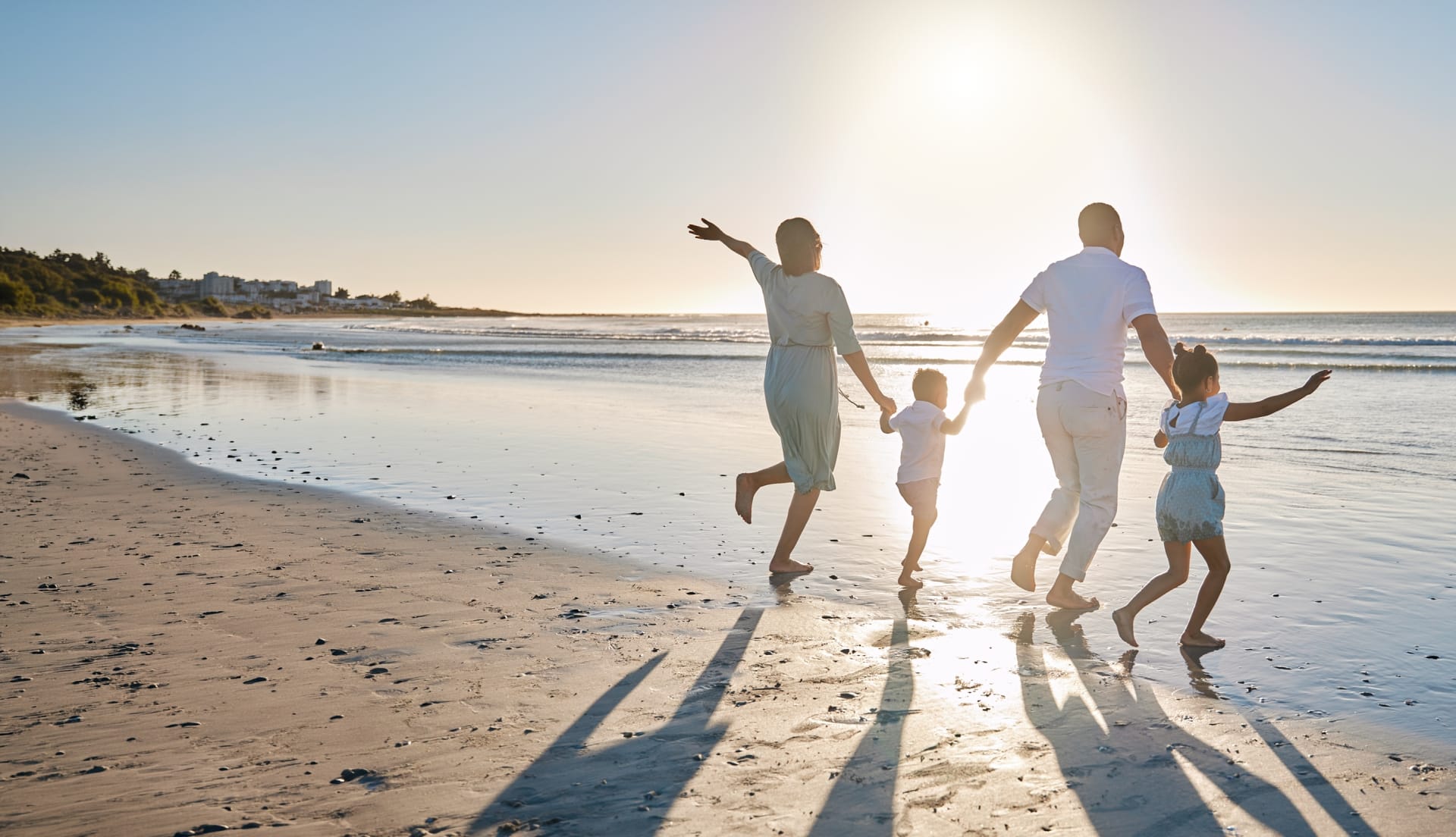 happy family holding hands walking toward low tide beach