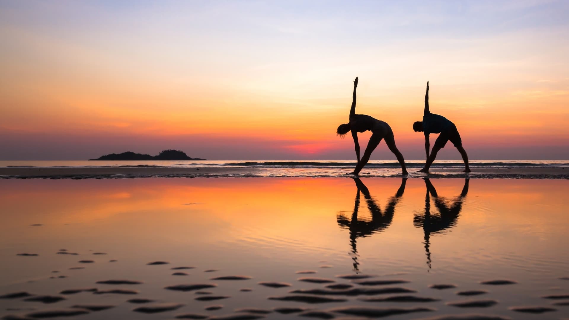 two people doing yoga poses on beach at sunset