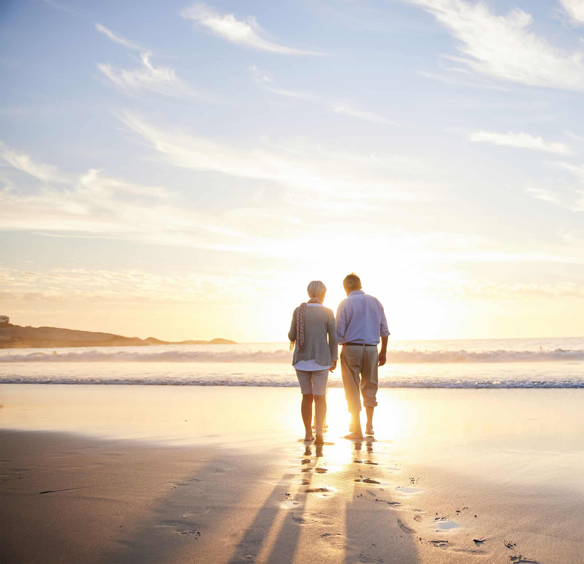 two older people walking on the beach at sunset
